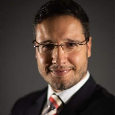 Profissional de negócios sorridente com óculos, promovendo o Acelerador Comercial, programa de crescimento e desenvolvimento de vendas.